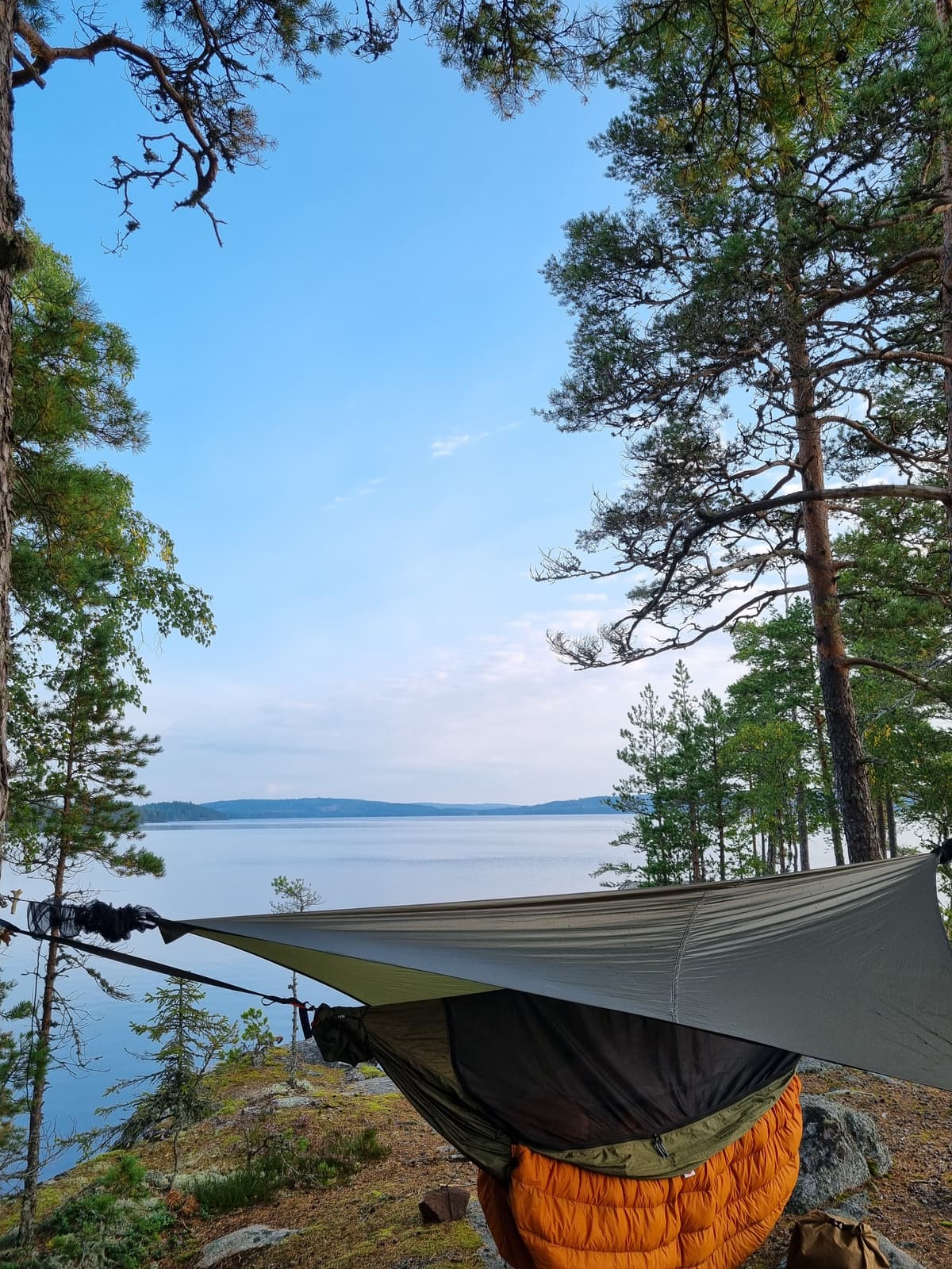 A hammock with a tarp setup close to a lake.