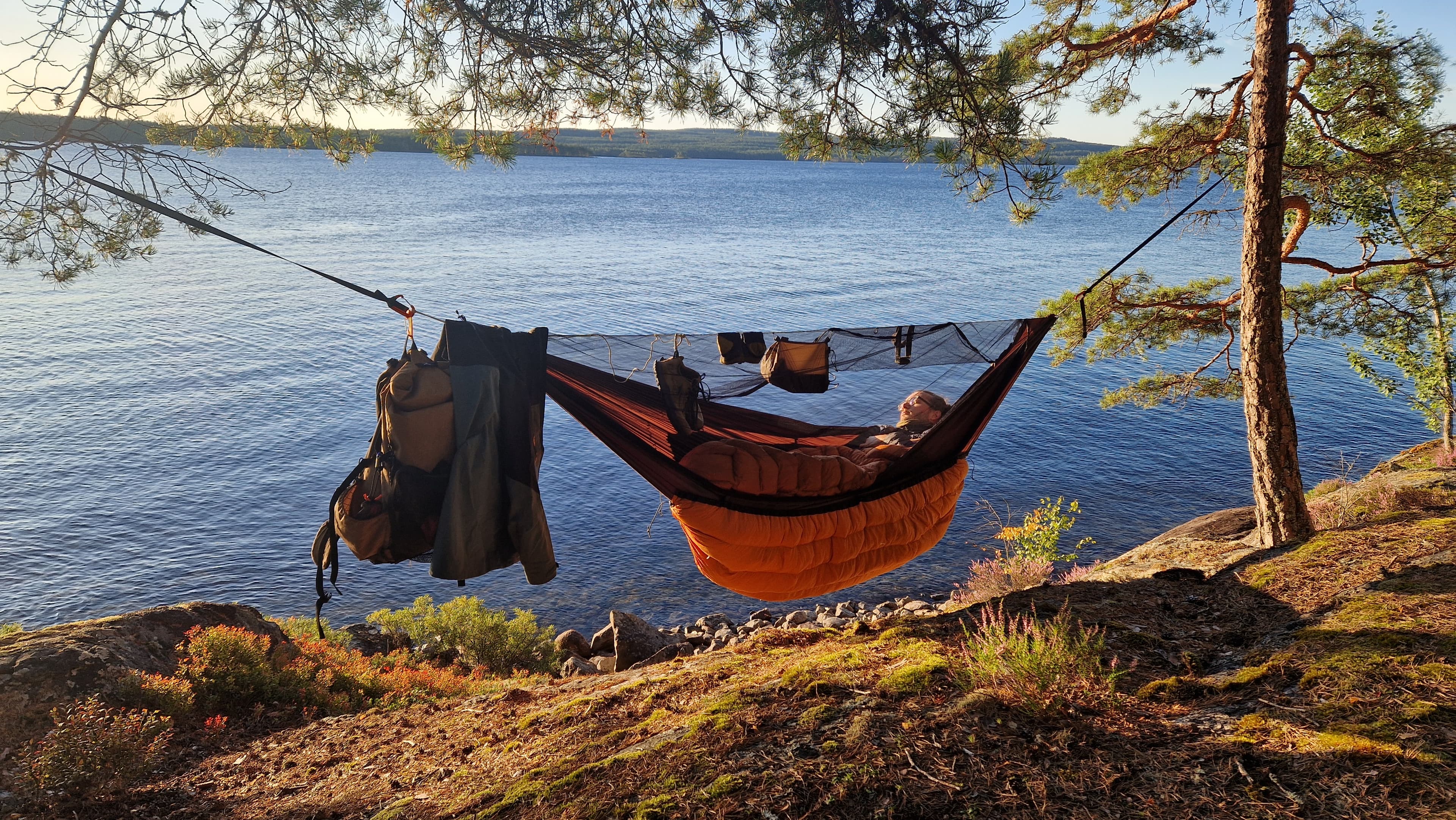Person in a hammock waking up near a lake.