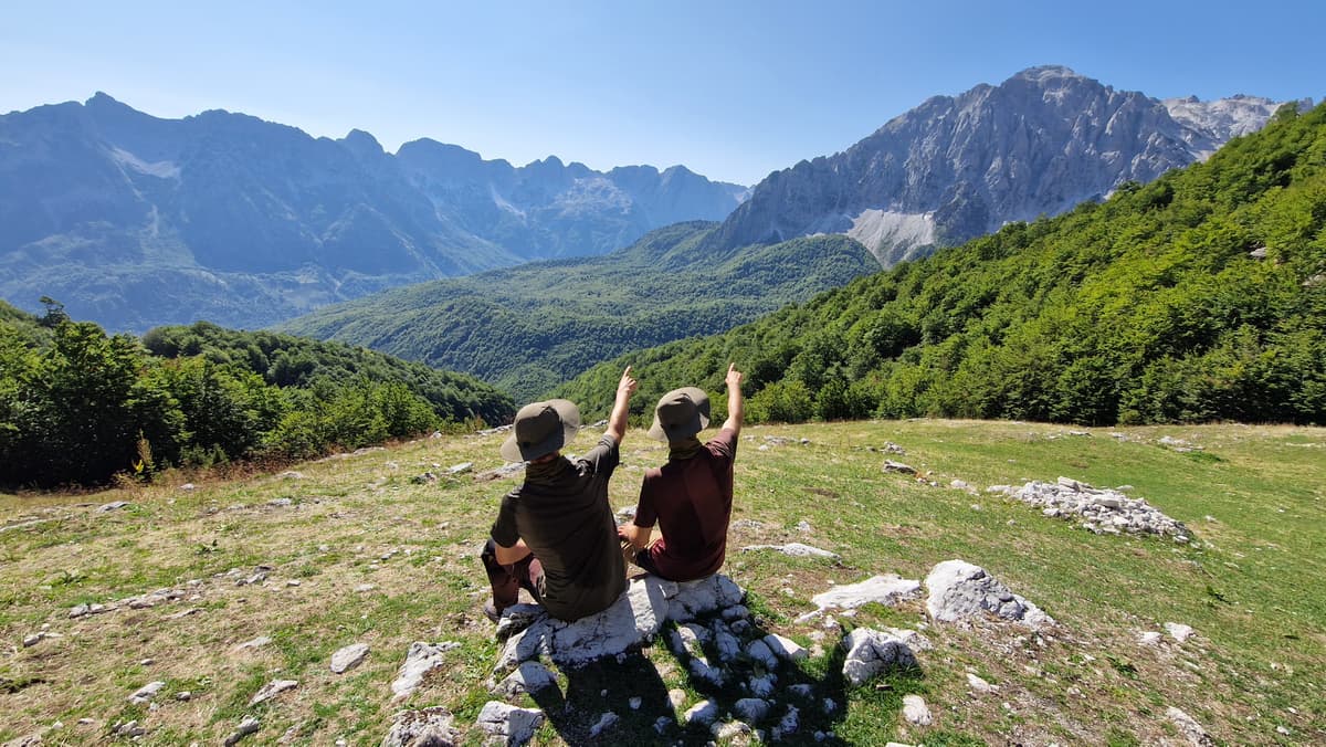 Two persons sitting on a rock pointing at a mountain.