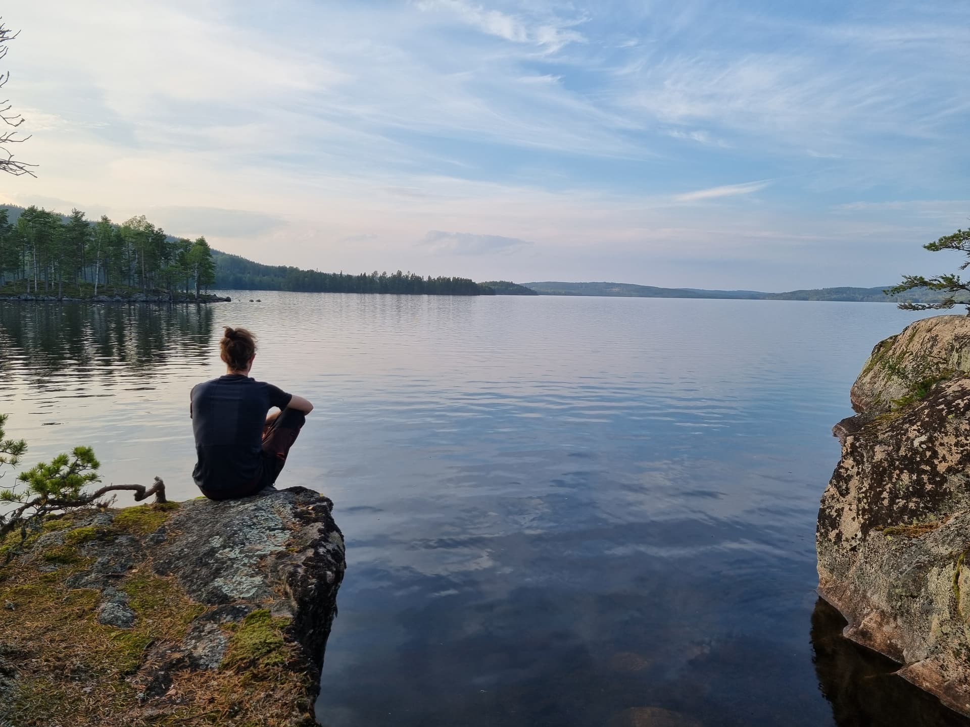 Person sitting on a rock, looking out over a lake in Glaskogen, Sweden