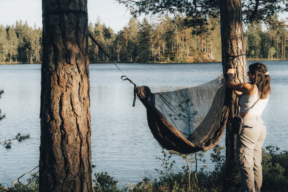 Person setting up hammock near a lake.